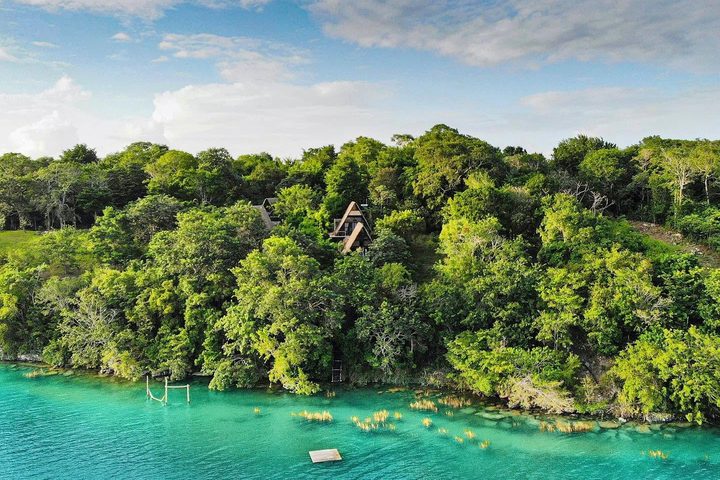 Vista aérea de la orilla turquesa de la laguna de Bacalar y de la selva donde asoman las cabañas de Azul Nomeolvides.