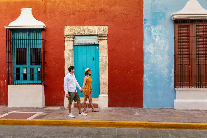 Una pareja pasea frente a fachadas roja y azul del centro histórico de Campeche.