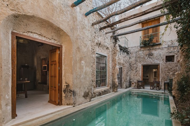 Patio de Casa Zotz, una de las casonas de Casonas MX: alberca entre muros antiguos de piedra, vigas de madera y puertas abiertas a las habitaciones.